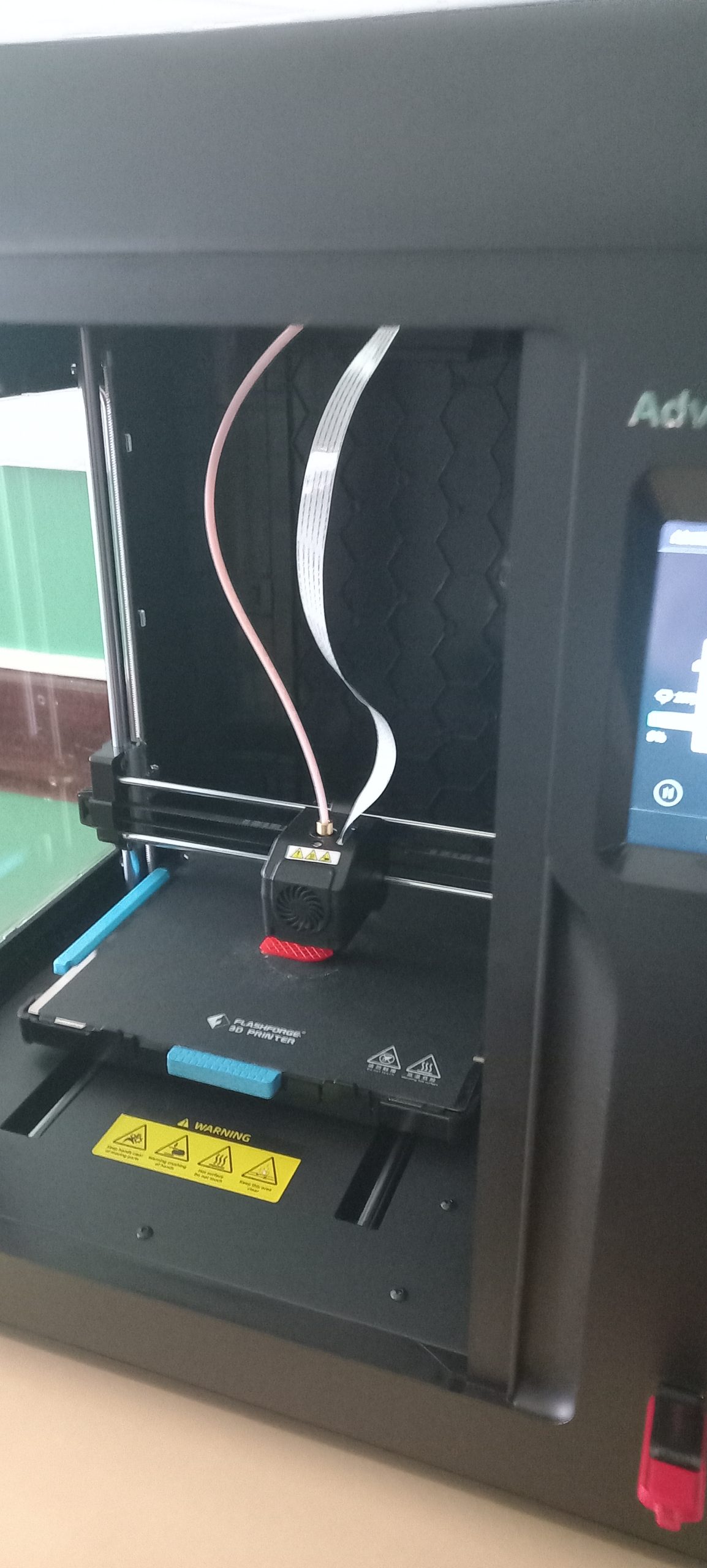 na zdjęciu widoczna drukarka 3D w trakcie drukowania czerwonego przedmiotu