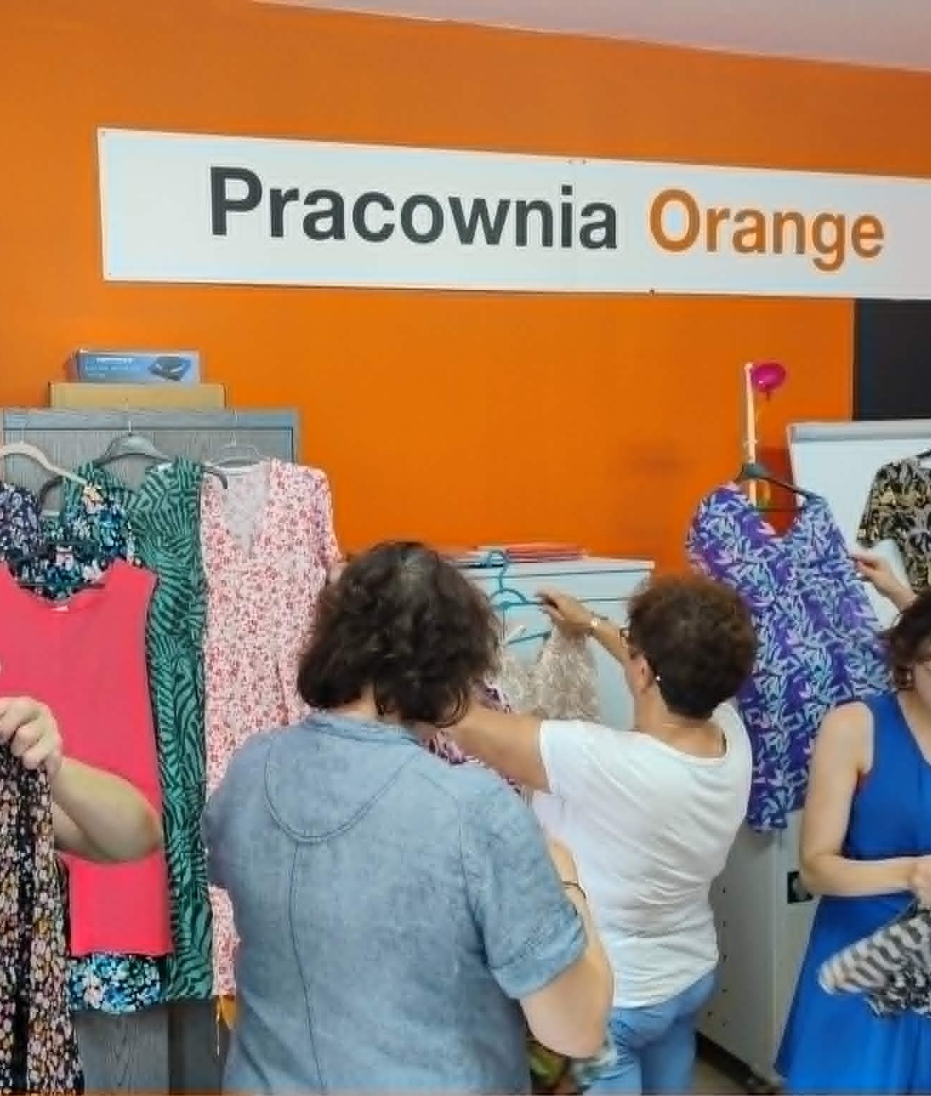 Grupa kobiet przegląda ubrania zawieszone na wieszakach.