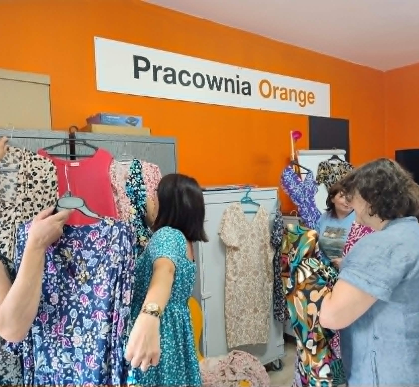 Grupa kobiet przegląda ubrania zawieszone na wieszakach.