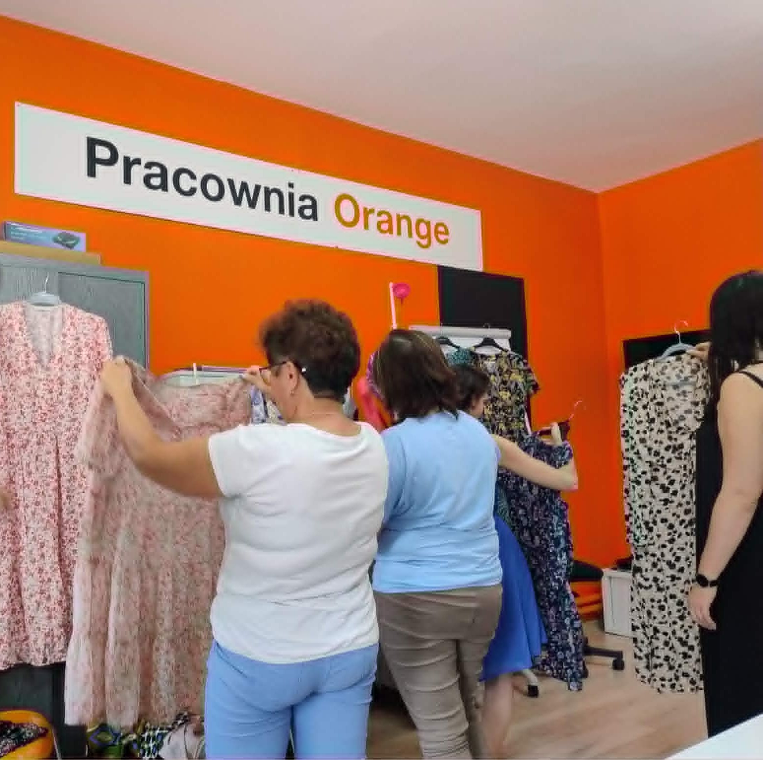 Grupa kobiet przegląda ubrania zawieszone na wieszakach.