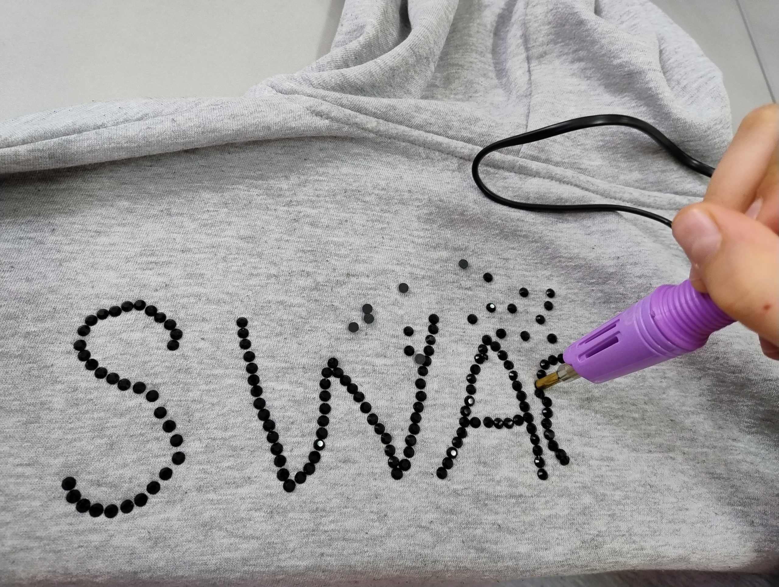 Osoba wykonuje ozdobę z cekinów na ubraniu.