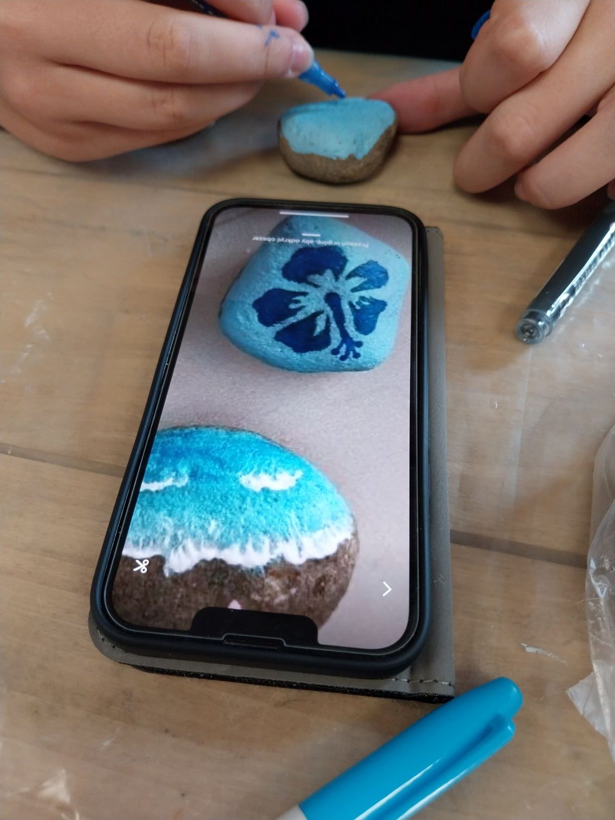 zabawa z kamykami. Uczestniczka korzysta z komórki i kopiuje obrazek na swój kamyk