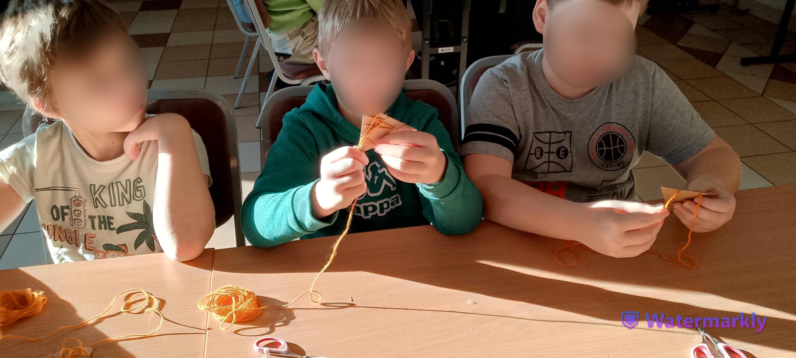Trzech chłopców owija pomarańczową włóczką kartoniki tworząc liska.
