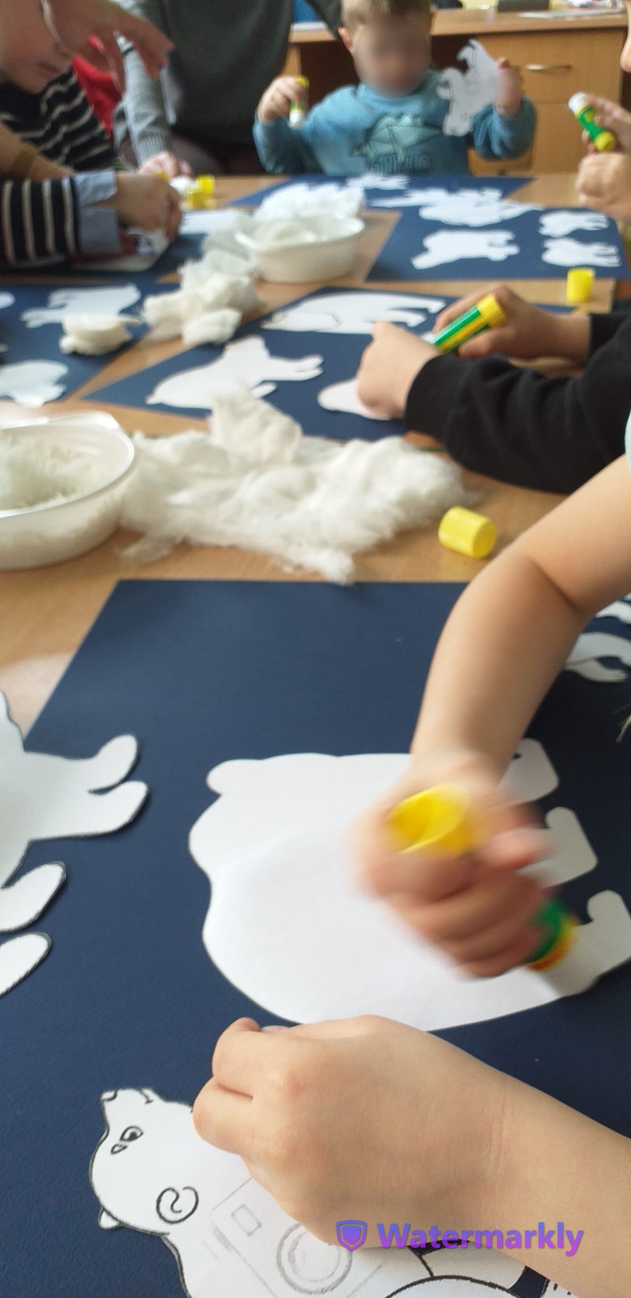 Dzieci przyklejają szablony niedźwiedzi do granatowych kartek.