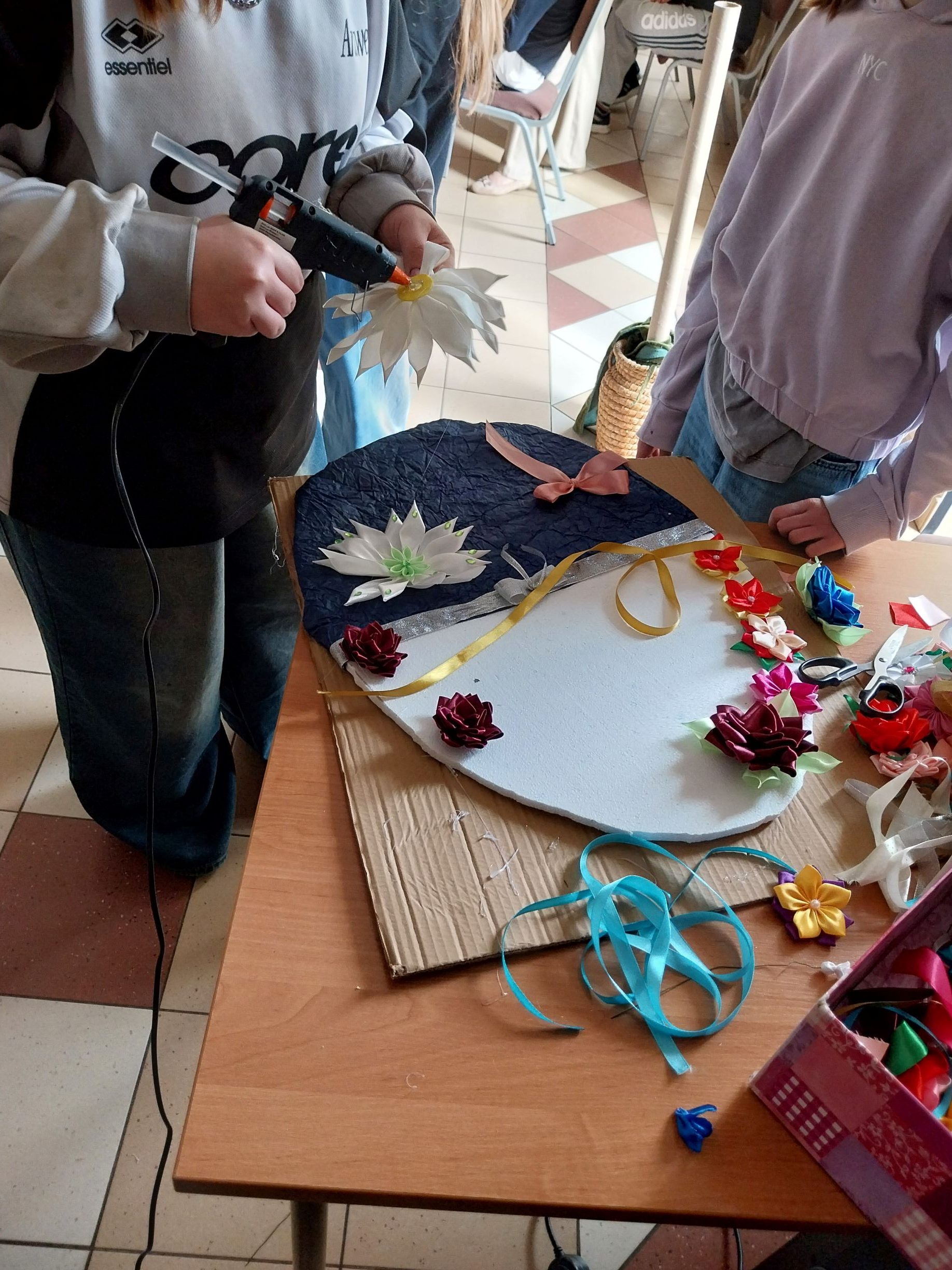 Dwie dziewczynki ozdabiają kolorowymi wstążkami styropianową formę jajka.