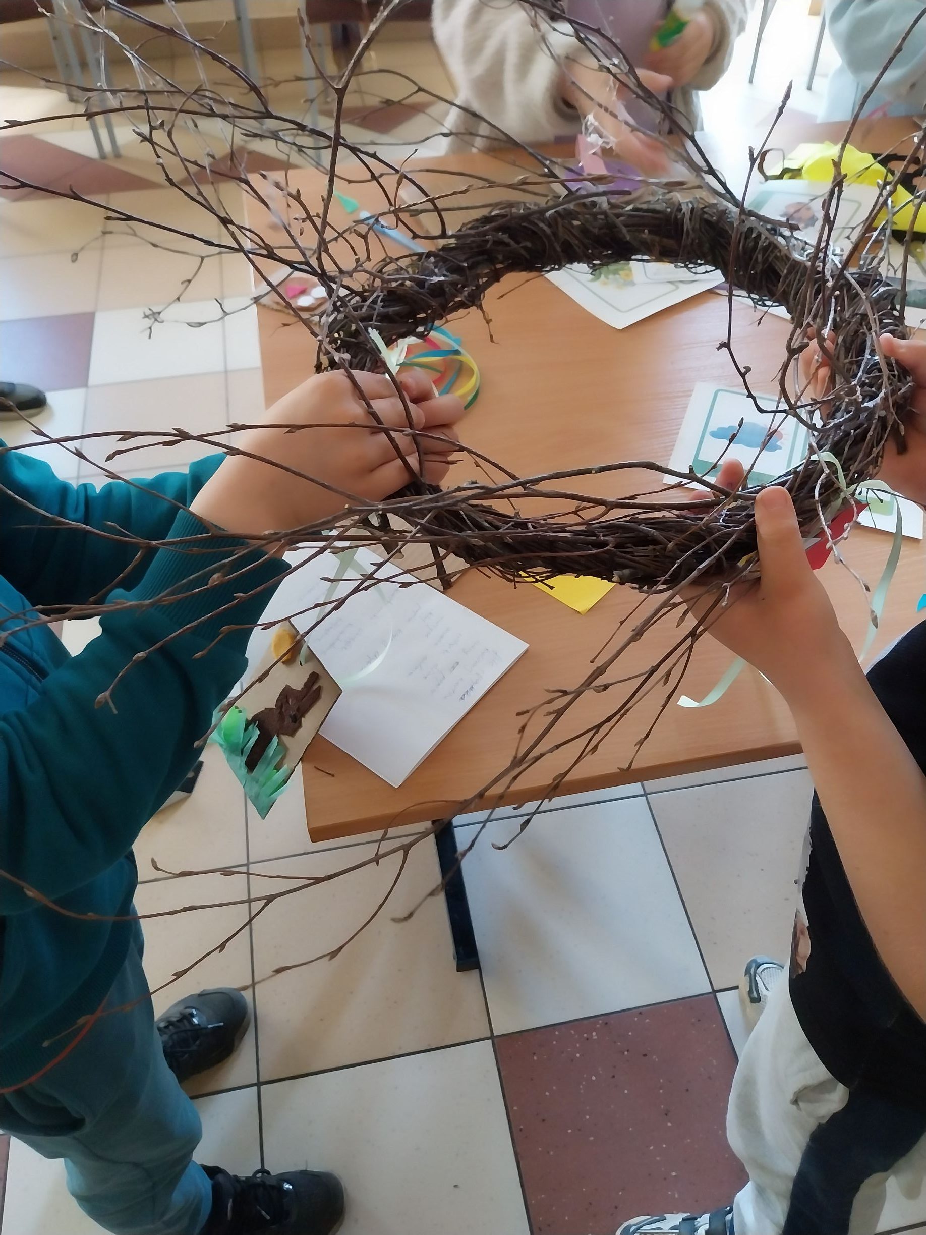 dwoje chłopców plecie bocianie gniazdo z witek brzozowych