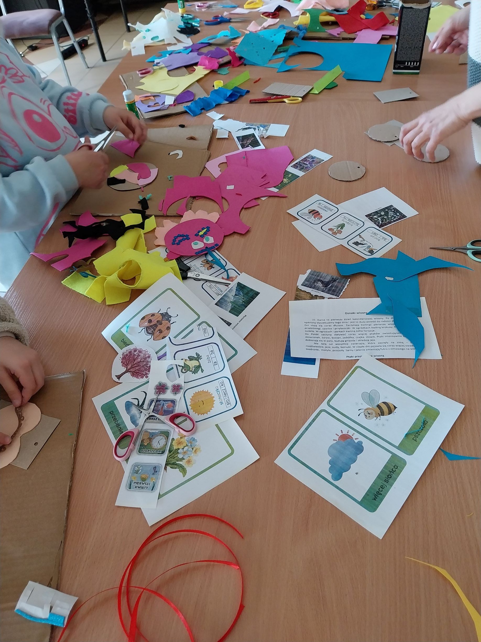 na stole leżą karty pracy - podpowiedzi oraz widać ręce dziewczyny, która tworzy kolejny element na nasz totem