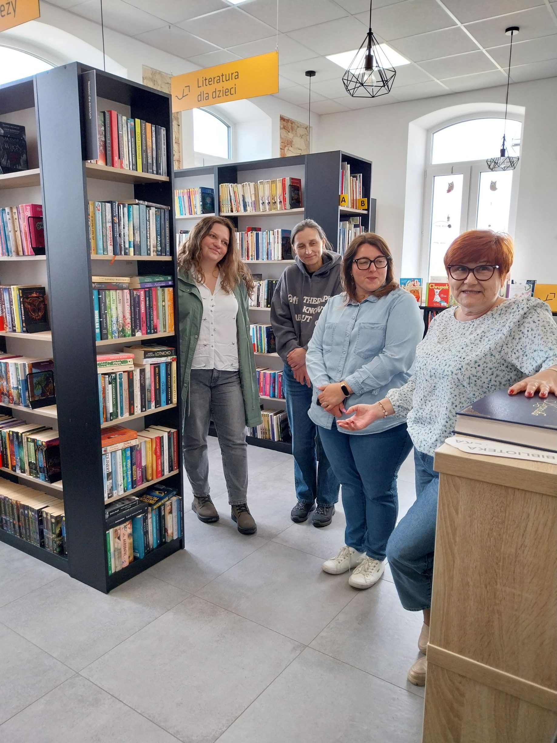 Grupa uczestników wizyty studyjnej zwiedza bibliotekę w Jabłonnie. Wita ich dyrektorka