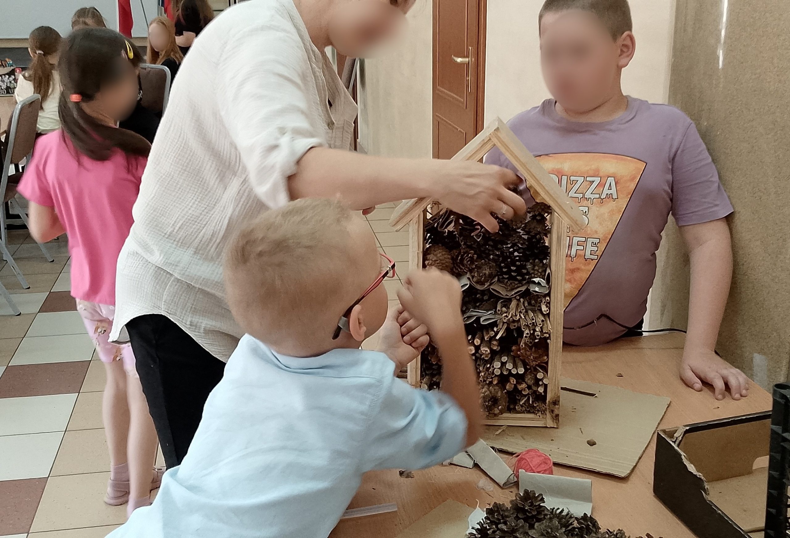 Dwaj chłopcy pomagają przy układaniu szyszek w domku dla owadów.
