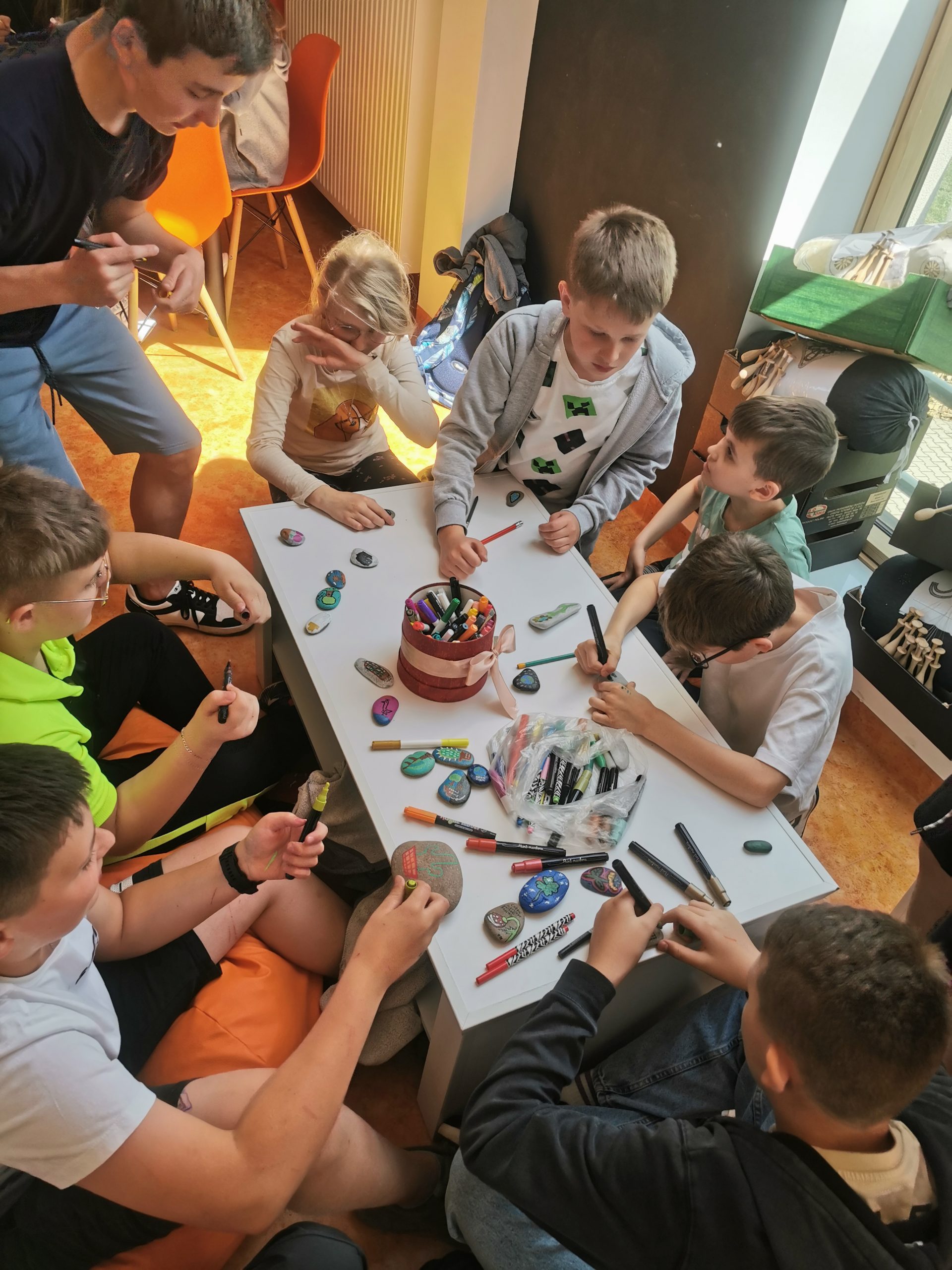 Kolorowe zdjęcie. Grupa dzieci maluje kamienie.
