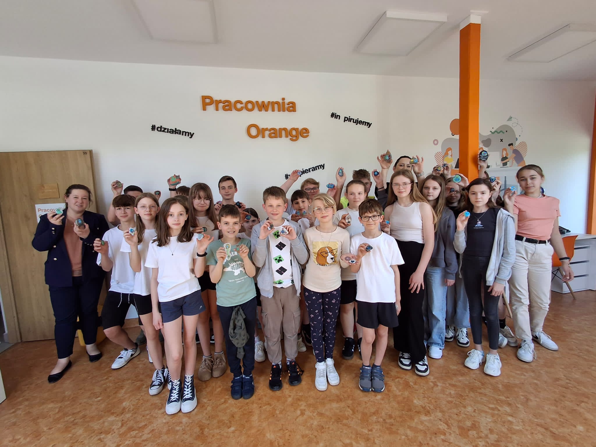 Kolorowe zdjęcie. Grupa młodzieży pozuje do zdjęcia z pomalowanymi kamieniami w Pracowni Orange.