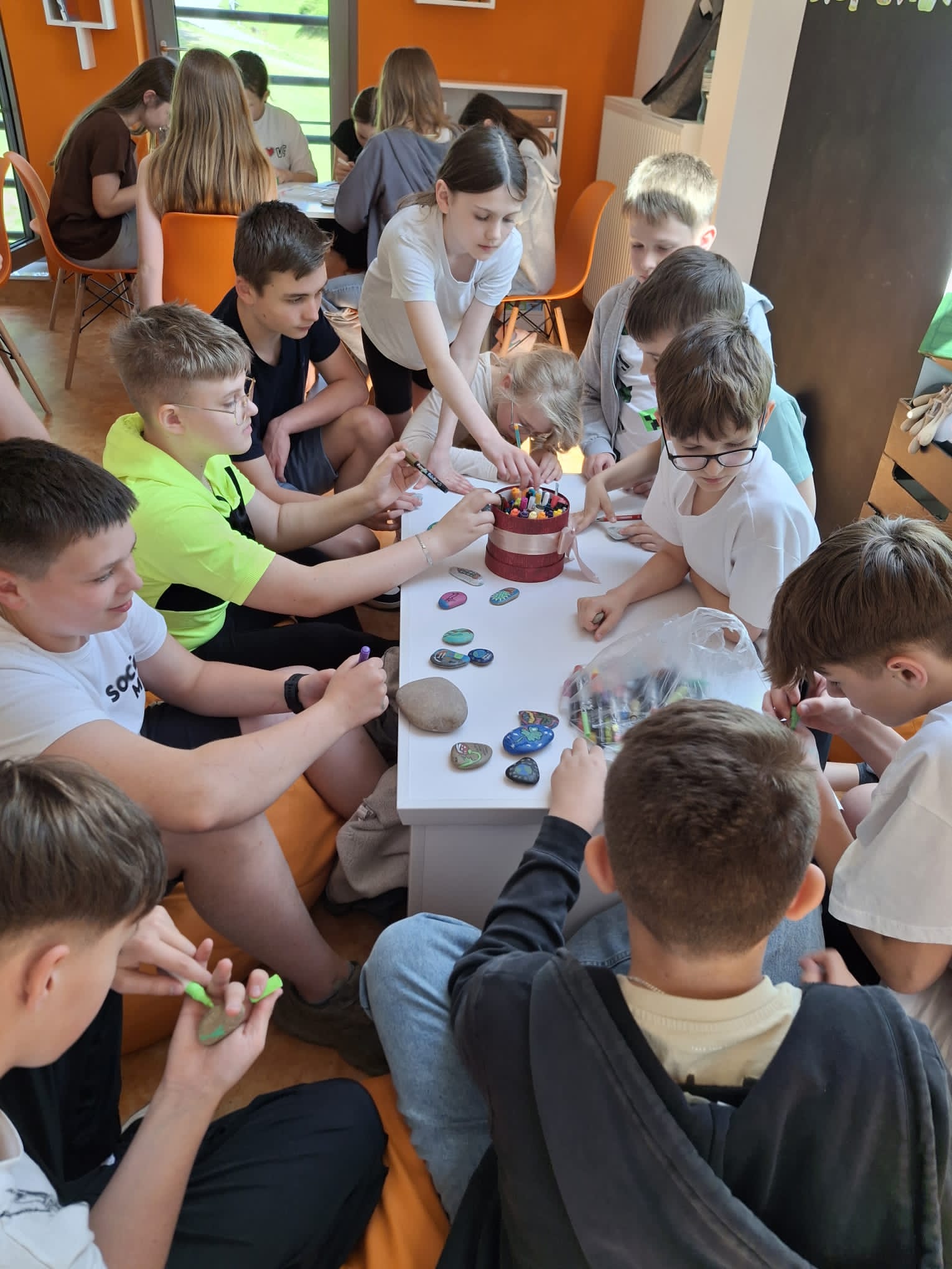 Kolorowe zdjęcie. Grupa młodzieży maluje kamienie.