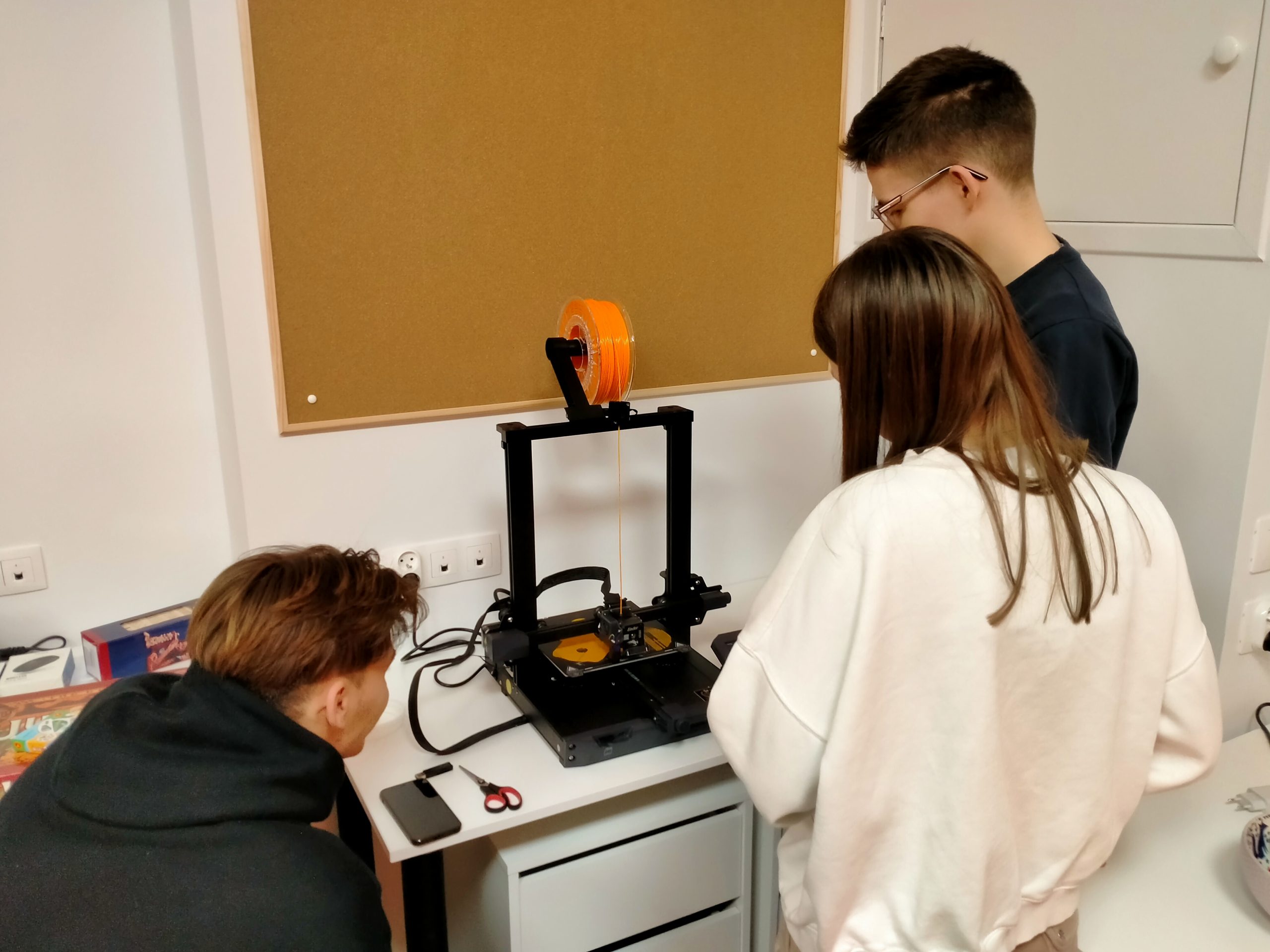 Trzy osoby obserwujące pracę drukarki 3D.
